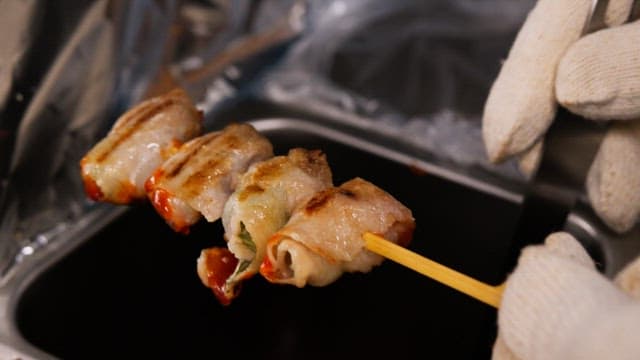 Gloved hands brushing sauce to grilled skewers in the kitchen