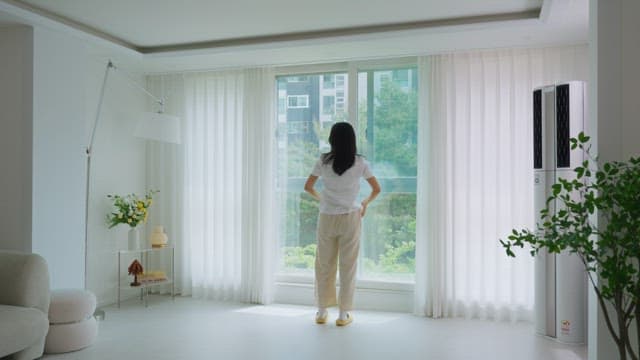 Woman looking out a window in a bright living room