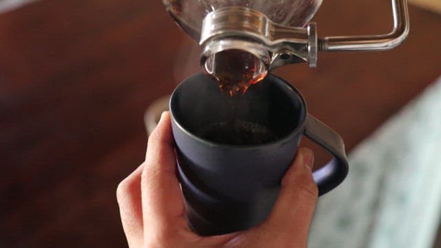 Hands pouring hot coffee into a cup in a cozy indoor setting