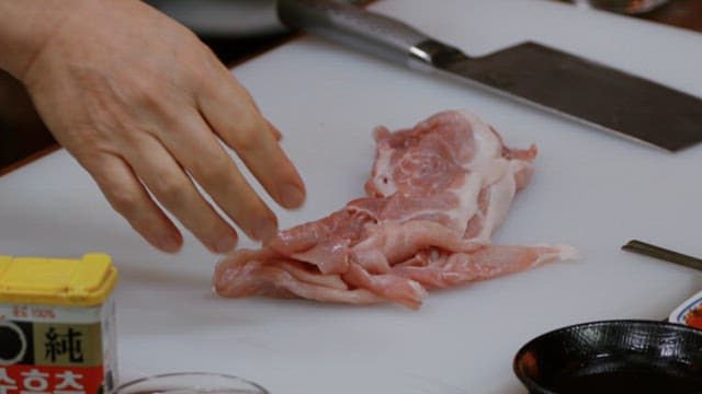 Preparing thin slices of raw pork on a cutting board