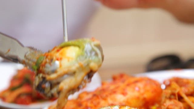 Tongs holding abalone in braised spicy seafood