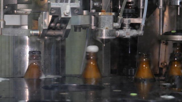 Automated machine putting caps on glass bottles containing beer in a factory