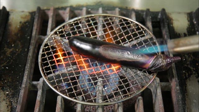 Grilling eggplant using a torch over fire