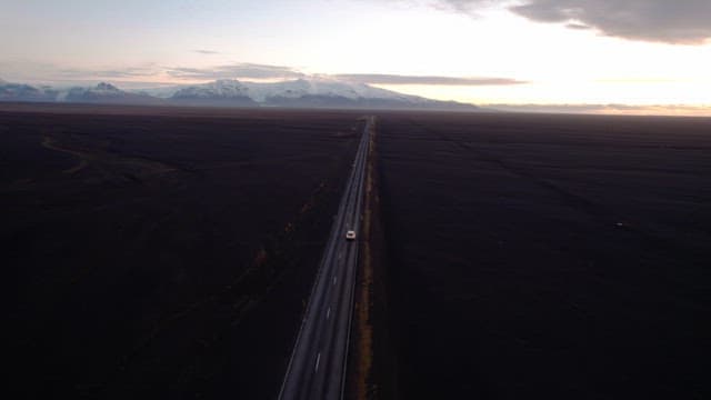 Car driving on a long road under a sunset sky