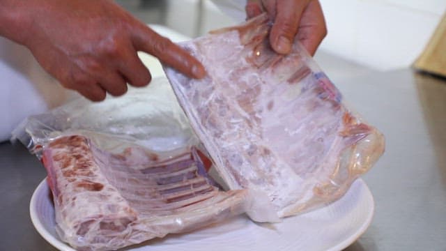 Person handling frozen rib racks in the kitchen