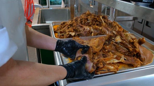 Preparing boiled meat on a metal tray with gloved hands