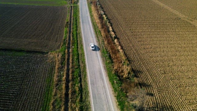 Car Traveling on Rural Road Between Farmlands