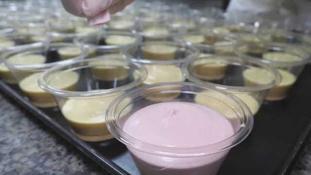 Pouring pink mousse into a plastic container containing yellow mousse