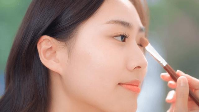 Woman applying eye makeup with a brush in a brightly lit room