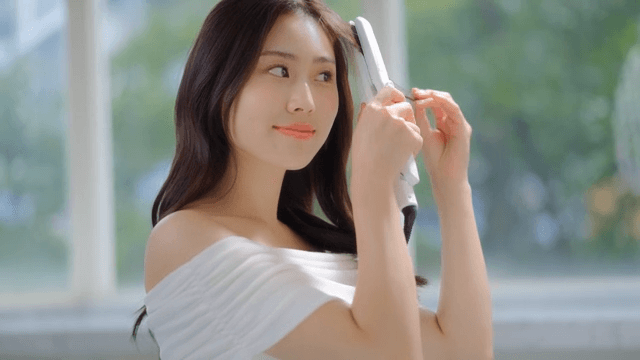 ㅉoman styling her hair with hair straightener indoors near a window