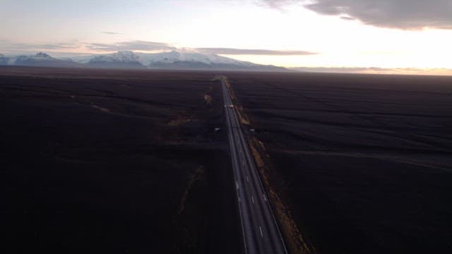 Car driving on a long road under a sunset sky