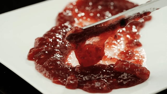 Spreading strawberry jam with a butter knife on a white plate