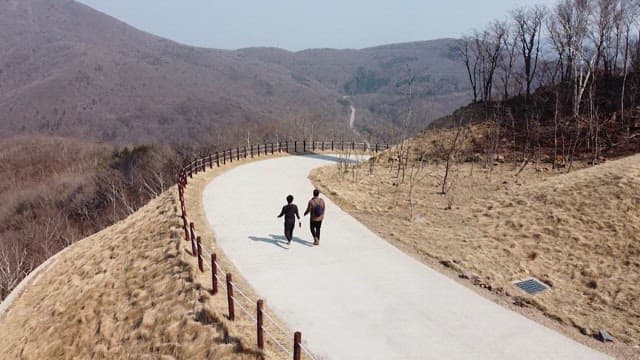 Two people walking along a mountain path lined with wind turbines
