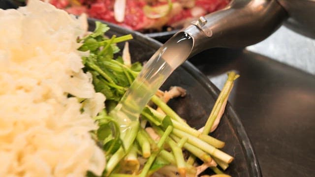 Pouring Broth onto Fresh Vegetables and Mushrooms for Cooking Hotpot