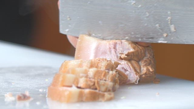 Slicing boiled pork slices on a cutting board with a knife in a kitchen