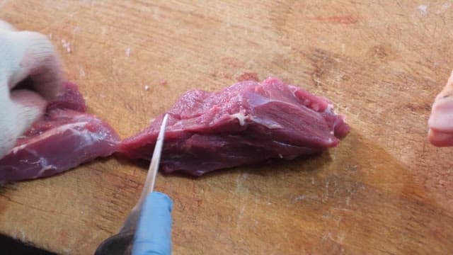 Cutting raw meat on a wooden board with gloves on