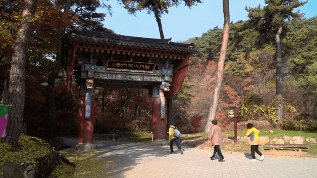 Tourists walking through a traditional wooden gate in a forest park during autumn.