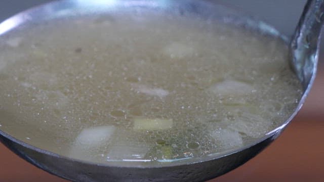 Ladle pouring hot broth of Samgyetang with chicken and vegetables using a ladle