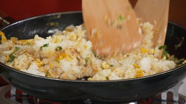 Cooking fried egg rice in a pan with wooden utensils