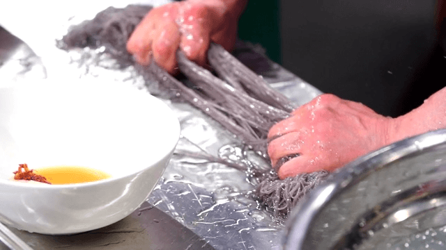 Chef preparing cold buckwheat noodles on a metal surface