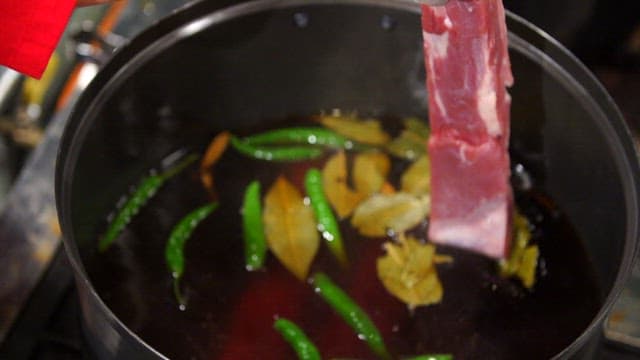 Pork being dipped into a pot with spices