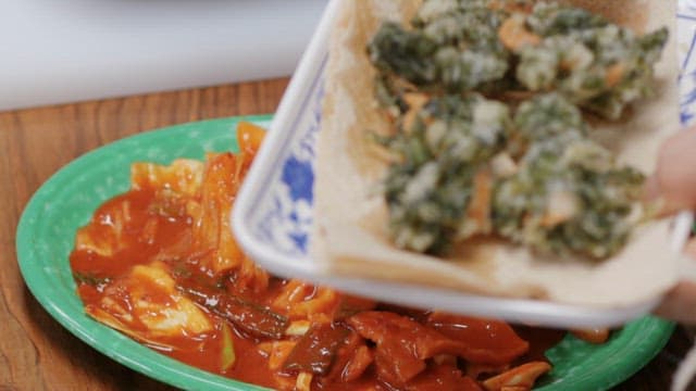 Serving fried vegetable fritters over spicy tteokbokki