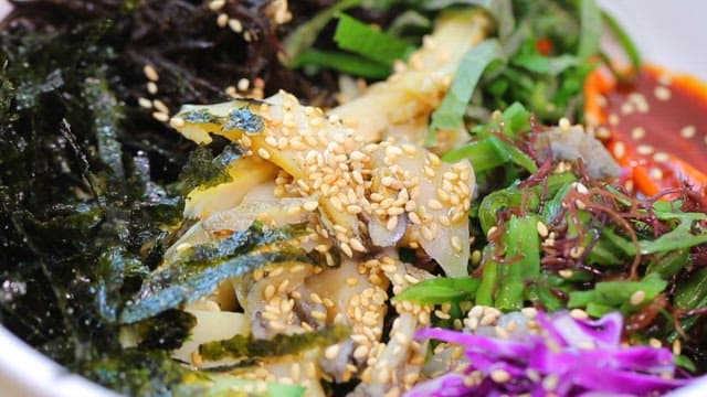 Mixing Korean bibimbap with fresh vegetables and abalone with spoon