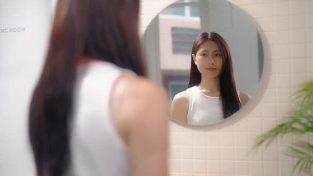 Woman drying her hair with a hair dryer in front of a bathroom mirror