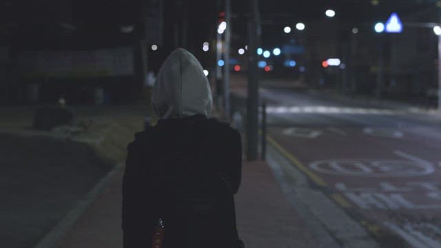 Person wearing a hooded jacket walking down a dimly lit urban street at night