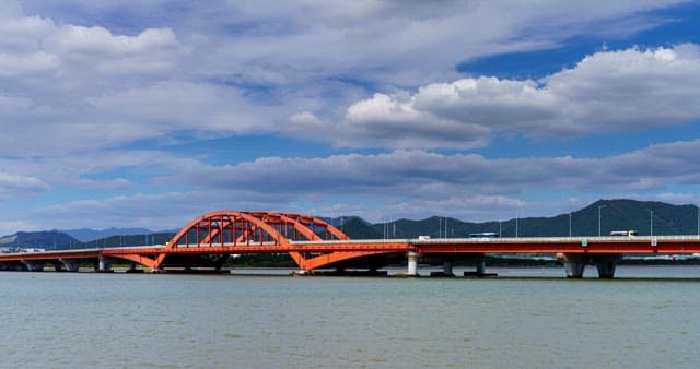 Red bridge crossing a sea under a cloudy sky