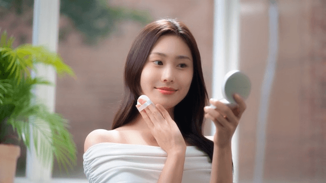 Woman in white top applying makeup with a mirror of cushion foundation