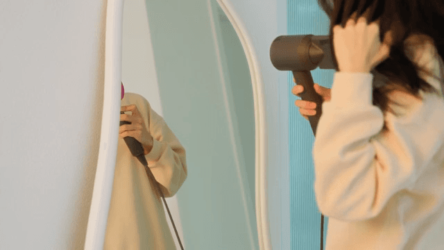 Woman drying her hair with dryer in front of a mirror