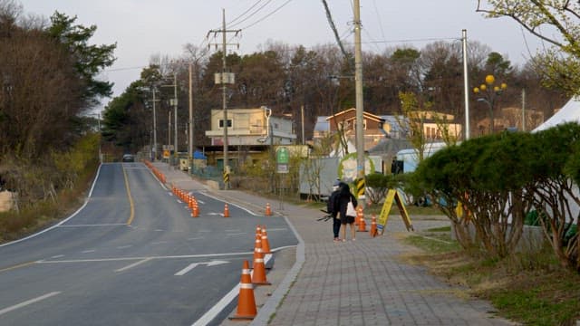 Two people walking along a roadside footpath in a suburban area