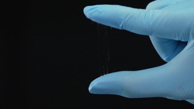 Gloved hand stretching a thin, transparent filament