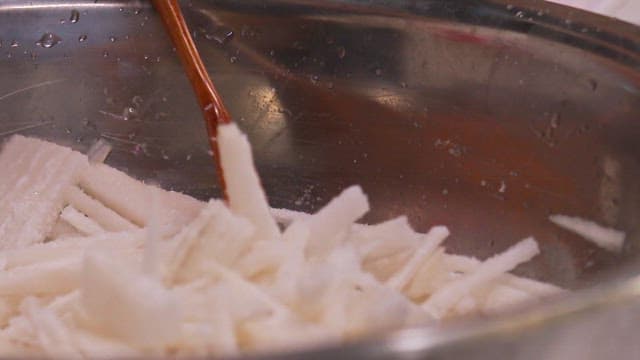 Mixing radish slices in a metal bowl