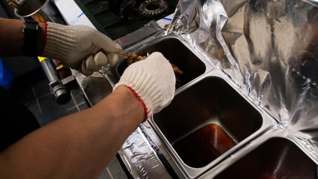 Gloved hands brushing sauce to grilled skewers in the kitchen
