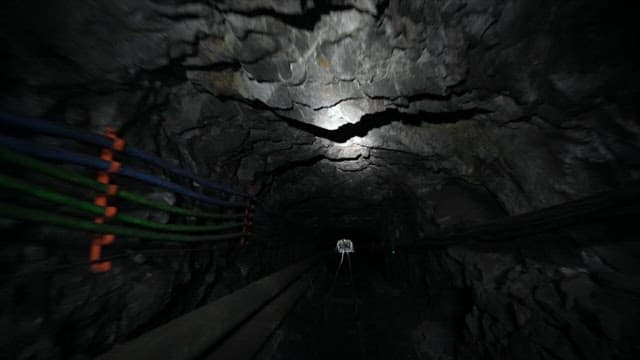 Narrow and dark mine tunnel with cables running along the walls