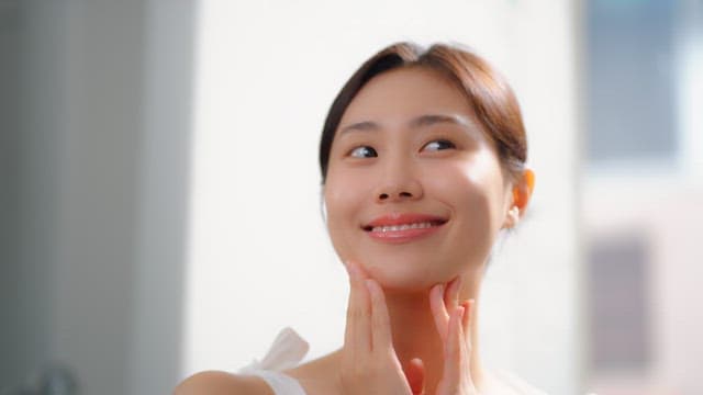 Woman smiling and touching her face in a bright room