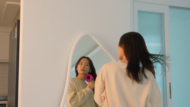 Woman drying her hair with dryer in front of a mirror