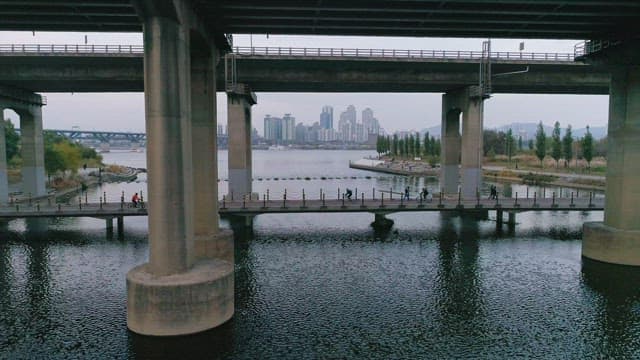 Riverside park under a bridge with city backdrop