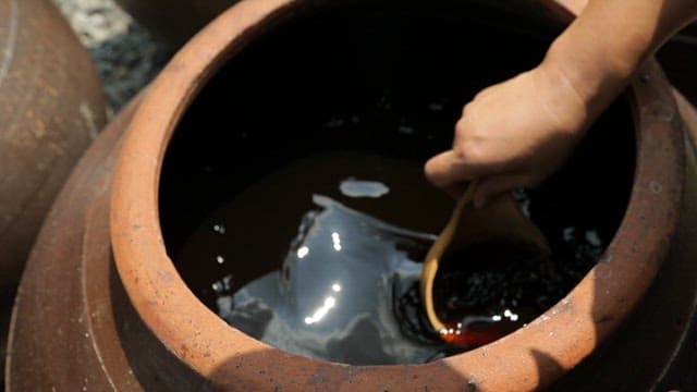Soy sauce being poured into a ladle from a traditional Korean jar