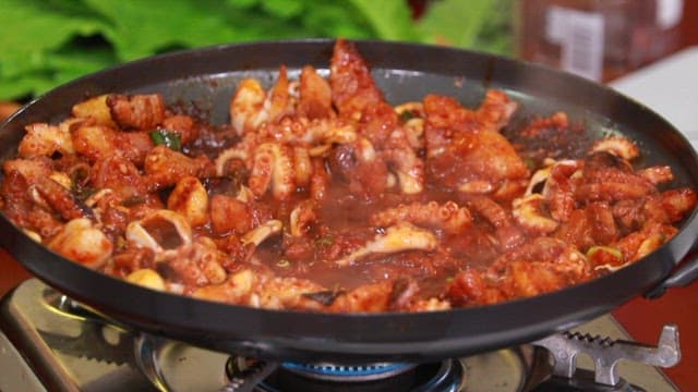 Stir-fried webfoot octopus and pork belly cooked in a pan on a gas burner