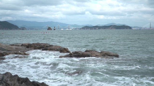 Rocky coastline with waves and a distant bridge