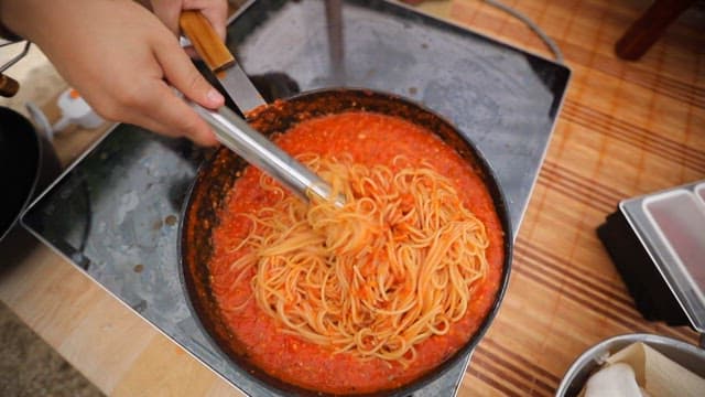 Mixing red pepper sauce and pasta noodles in a frying pan