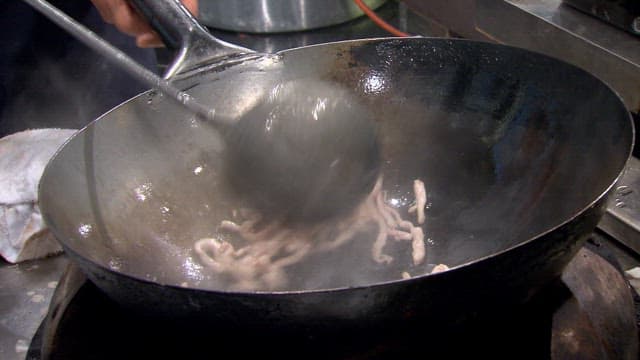 Chef stir-frying meat and vegetables in a hot wok in the kitchen