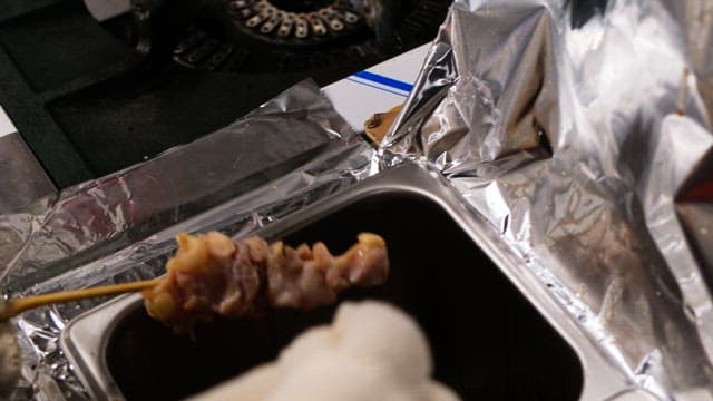 Gloved hands brushing sauce to grilled skewers in the kitchen