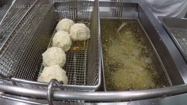 Putting potato croquette batter into a deep fryer full of oil in a commercial kitchen