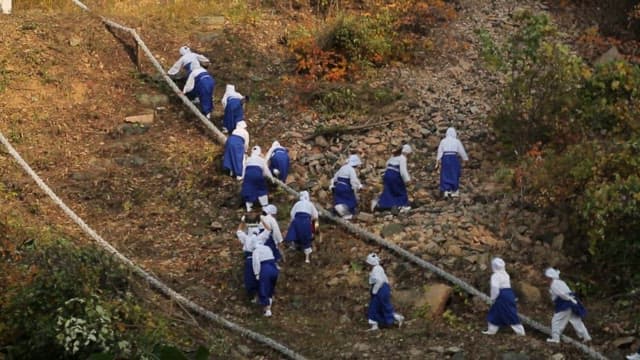 Women in traditional attire, Hnabok hiking up a rocky hil