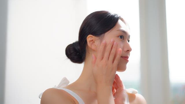 Woman smiling and touching her face in a bright room