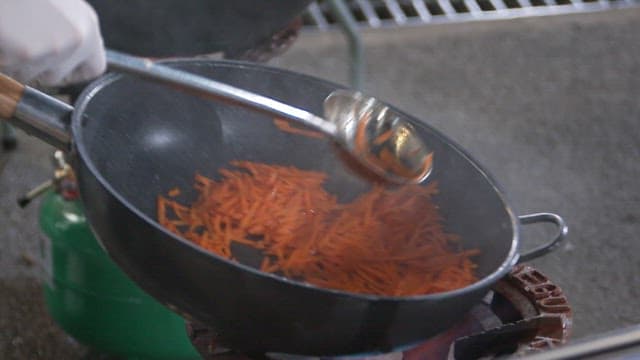 Stir-frying shredded carrots in a wok on a outdoor gas stove